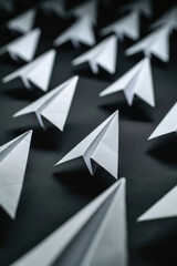 Group of white paper airplanes on black background. Suitable for business or travel concepts - obrazy, fototapety, plakaty