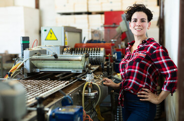 Confident woman machine operator working with automatic conveyor filling and seeding of plants in greenhouse nursery