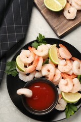 Tasty boiled shrimps with cocktail sauce, parsley and lime on light grey table, flat lay