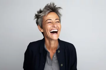 Fotobehang Portrait of a happy mature woman laughing against a grey background. © Igor