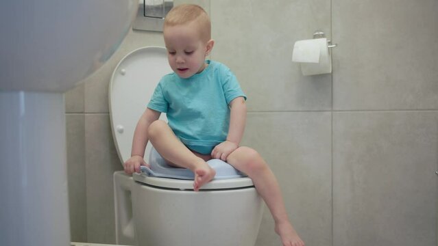 Cheerful toddler sitting on toilet looking at camera with innocence and curiosity candid moment in bathroom. Child sitting on toilet playful demeanor while boy sitting on toilet reflects joy