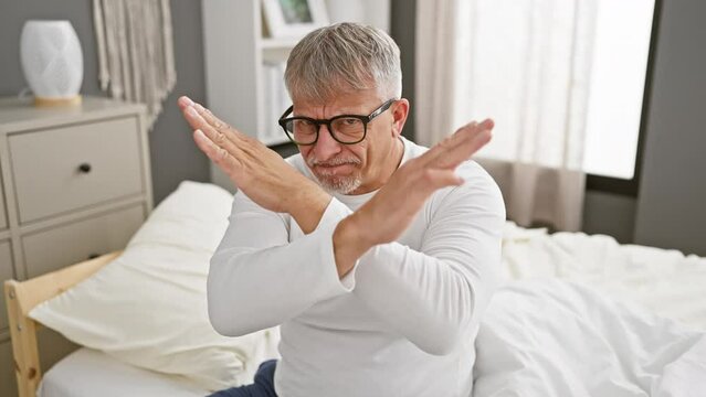 Rejection strikes home, a middle-aged, grey-haired man expresses angry rejection, wearing pyjamas and crossing arms in a bedroom setting