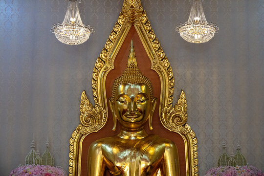 Portrait shot of Golden Buddha statue, Wat Traimit (temple of the Golden Buddha). Crystal Chandeliers, flowers on either side. 
