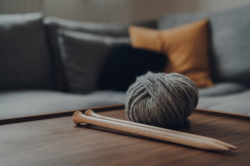 Ball of grey chunky wool yarn and a pair of large wooden knitting needles on a table.
