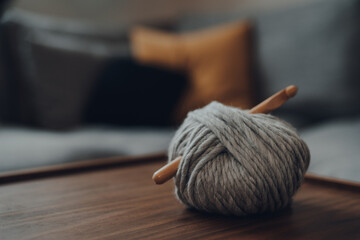 Ball of grey chunky wool yarn with a large wooden crochet hook on a table. - obrazy, fototapety, plakaty