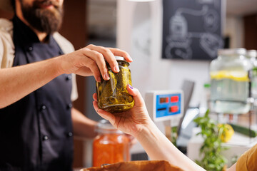 Close up shot of customer at checkout counter in zero waste shop, buying locally sourced ecofriendly vegetables from storekeeper. Client purchasing pickles jar in local neighborhood store