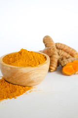 Raw turmeric material and powder in a wooden bowl