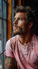 Obraz premium Contemplative man gazes out a window, light illuminating his tattooed arm and tousled hair