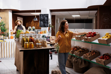 Green living woman in zero waste store interested in purchasing natural vegetables with high...