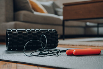 Jump rope and a foam roller on a fitness mat, modern living room, selective focus.