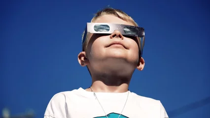 Foto op Canvas A young boy safely looks at a total eclipse while wearing protective glasses.    © Orlowski Designs LLC