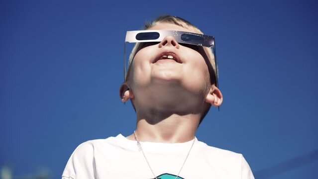 A young boy safely looks at a total eclipse while wearing protective glasses.  	
