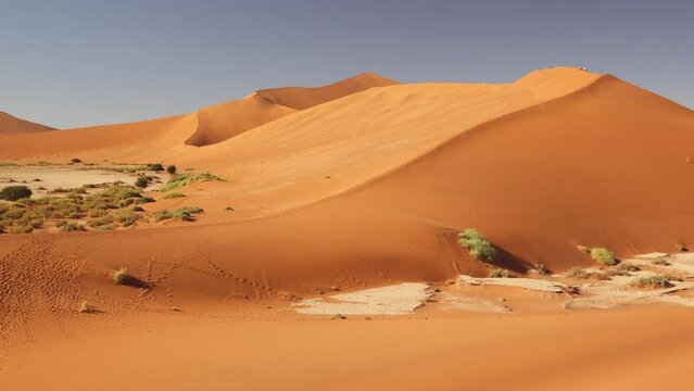 Large red sand dune in morning warm light in Sossvlei, Deadvlei, Namibia, Africa. Small group ik walkers, hikers on top, summit of rolling hill of dust and sand