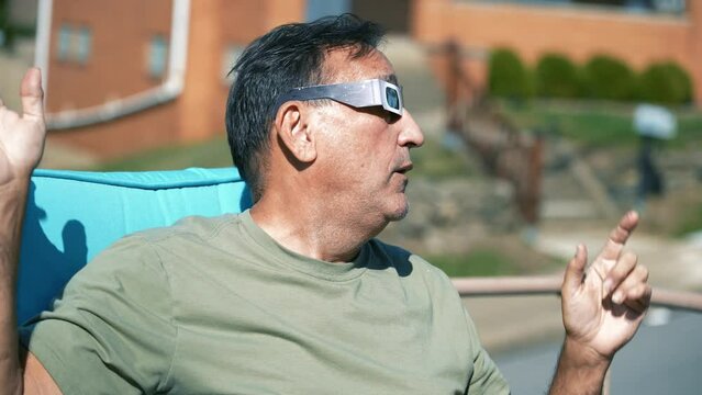 A man looks at a total solar eclipse while wearing protective eclipse sunglasses.  	