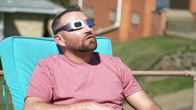 A slow motion view of a man eating popcorn while looking at a total solar eclipse while wearing protective eclipse sunglasses.  	