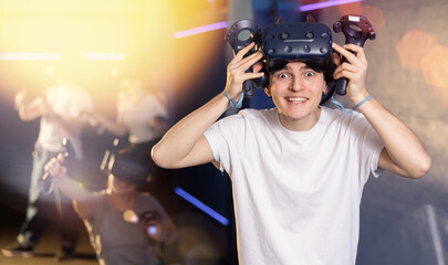 Portrait of happy excited young guy with VR glasses on head, holding handheld controllers playing...