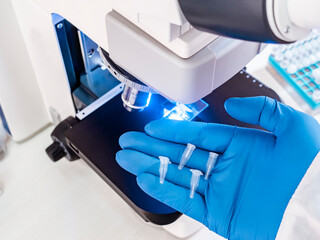Small PCR tubes in the hand of a scientist against a background of blue light near a microscope.