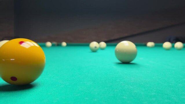 4K video. Yellow glossy shiny ball with red dot hits white ball with number 8 on green pool table. Club for playing billiards. Player pockets the ball. Closeup. Concept of hobby, sports, betting, bar