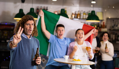 Cheerful sports supporters rejoicing winning game with flag of Italy, beer and snacks in evening pub
