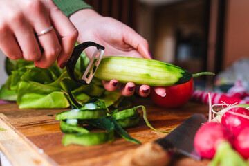 A close up of girl's or woman's hands peeling and cutting vegetables with knife making salad	

