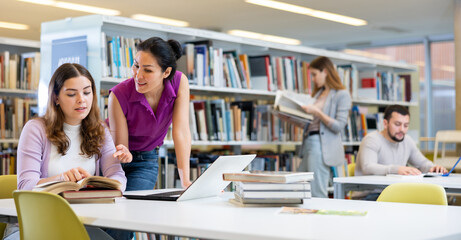 Two female students preparing a report on a laptop in the university library are looking for...