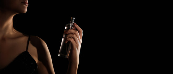 Pretty woman with bottle of perfume on black background