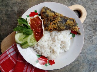Lele krispi or crispy catfish. The catfish is seasoned and then fried in a flour coating. Served with rice, chili sauce and fresh vegetables. Top view.