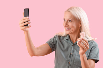 Mature woman with vibrator taking selfie on pink background