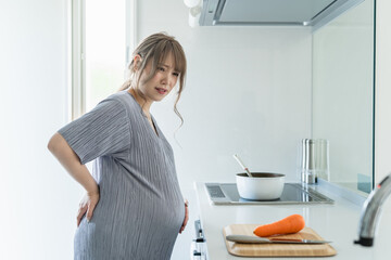 キッチンで腰痛に苦しむ妊娠後期の妊婦の女性
