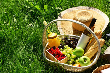 Set for romantic picnic with wicker basket full of tasty food and drinks on grass in park
