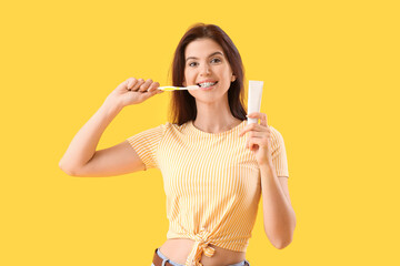 Young woman with dental braces brushing teeth on yellow background