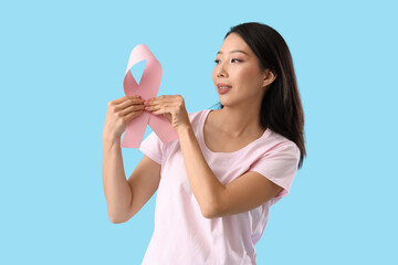 Young Asian woman with pink ribbon on blue background. Breast cancer awareness concept