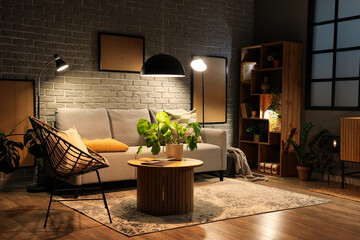 Interior of modern living room with grey sofa, wooden coffee table and glowing lamps at evening