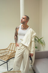 Chico joven tatuado y musculoso posando con ropa contemporánea en el hall de un hotel 