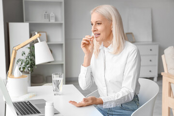 Mature woman taking pills at workspace in living room