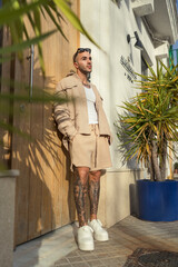 Hombre joven tatuado y fitness posando en la entrada y hall del hotel donde viaja con ropa urbana...
