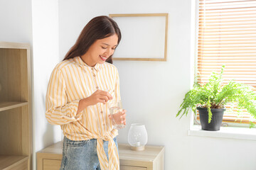 Young Asian woman with glass of water taking pills at home