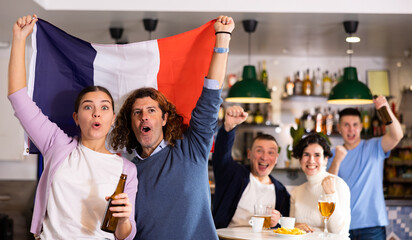 Company of enthusiastic young adult sports fans waving flag of France and supporting national team...