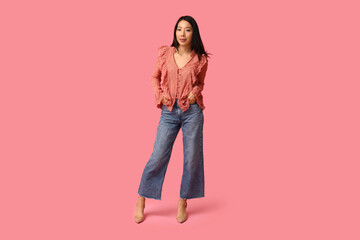 Fototapeta premium Beautiful young happy Asian woman in stylish jeans on pink background