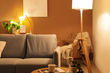 Interior of modern living room with grey sofa and glowing lamps at evening - obrazy, fototapety, plakaty