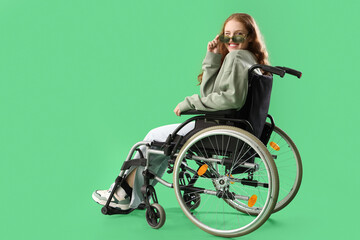 Young redhead woman in wheelchair with sunglasses on green background