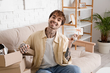 Young tattooed man with gift card and new shoes sitting on sofa at home