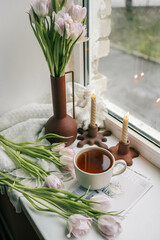 Cup of tea, bouquet of pink tulips and candles, spring aesthetics