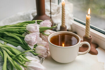 Cup of tea, bouquet of pink tulips and candles, spring aesthetics