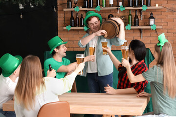 Young people with pouring beer from barrel to his friends in bar on St. Patrick's Day