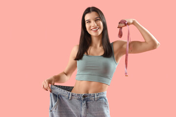 Young woman in loose jeans with tape measure on pink background. Diet concept