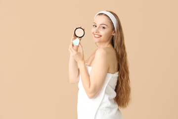 Beautiful young woman with heart-shaped sponge and makeup powder on beige background