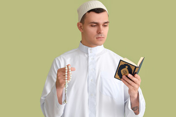 Young Muslim man with praying beads and Koran on green background. Ramadan celebration