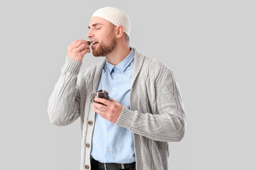 Young Muslim man eating dates on light background. Ramadan celebration