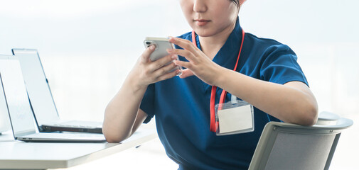 休憩時間にスマホを見るスクラブ姿の医療従事者の女性（顔なし）
